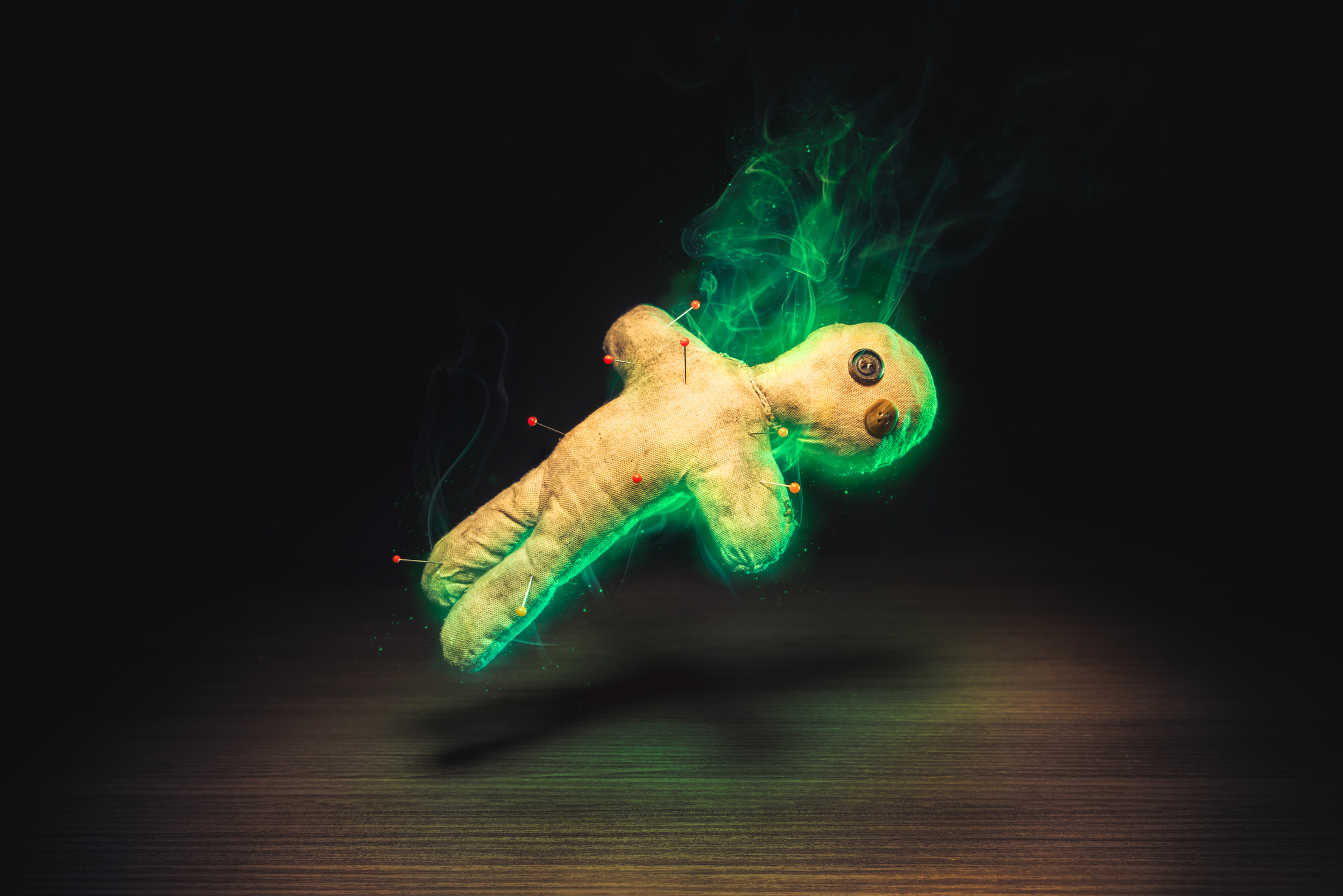Voodoo doll on wooden background levitating in green